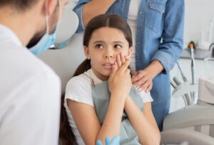 small client with dentist and pain in the teeth sitting in dental chair while mother standing near her for support