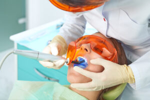 Girl child at the doctor. Dentist places a filling on a tooth with dental polymerization lamp in oral cavity. over clinic background.