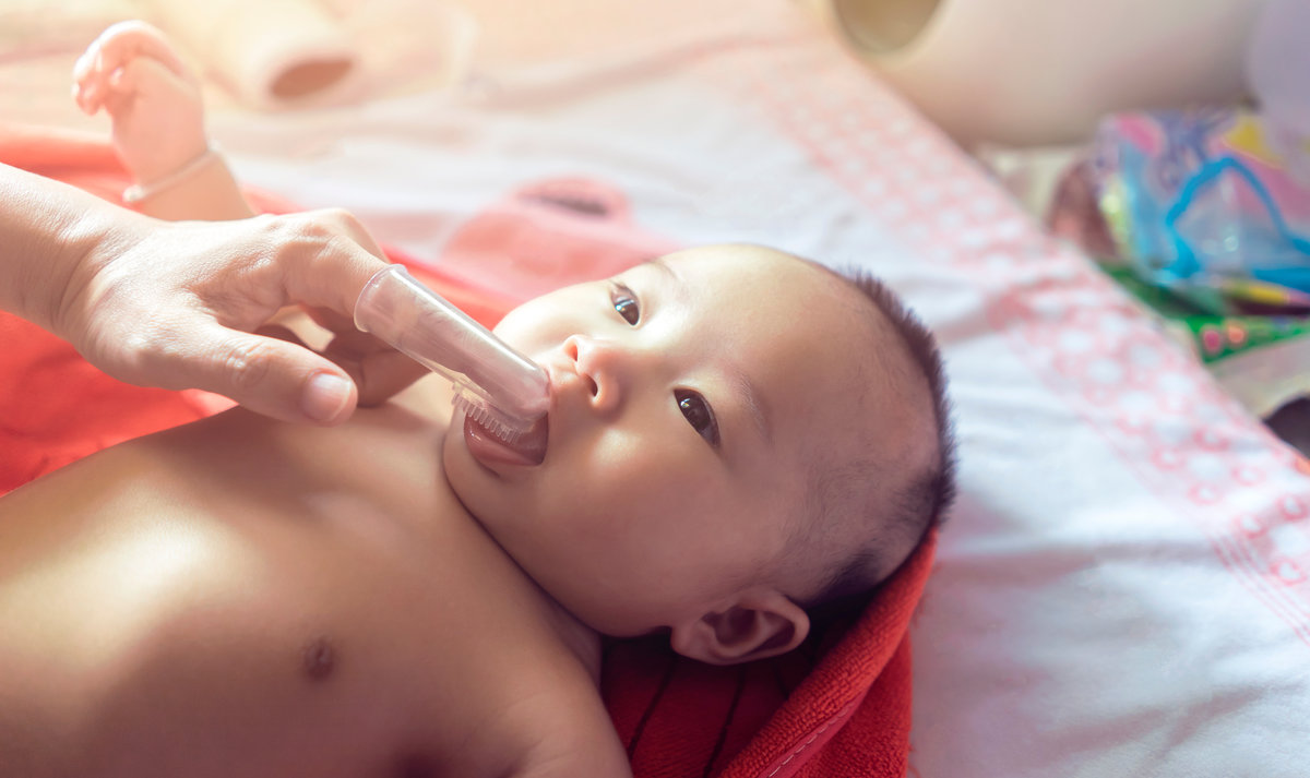 mother using finger wearing plastic baby toothbrush cleaning adorable baby tongue and mouth, parenthood motherhood raising kid child with love care kindness, keep clean hygiene looking after newborn